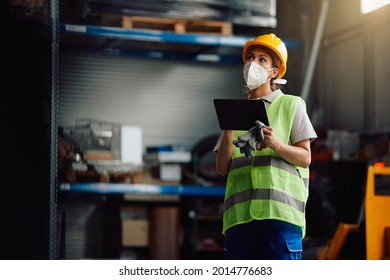 Female Worker Wearing Protective Face Mask While Working On Digital Tablet At Distribution Warehouse. 