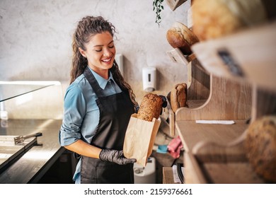 Female worker working in bakery. She packs the bread into a paper bag. - Shutterstock ID 2159376661