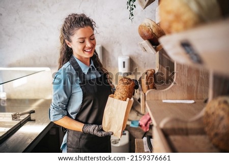 Female worker working in bakery. She packs the bread into a paper bag.