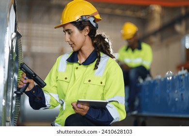 Female Workers in green uniforms and safety helmets perform quality checks inside a metal sheet factory. - Powered by Shutterstock