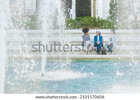 female workers talking while sitting in front of a fountain
