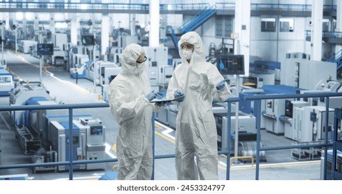 Female Workers Wearing Full-Body Polypropylene Coveralls at a Manufacturing Plant. Specialists Using Tablet Computer, Discussing Automated Work Process. Employees Protected From Hazardous Materials - Powered by Shutterstock