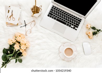 Female workspace with laptop, roses flowers bouquet, golden accessories, notebook, glasses. Flat lay women's office desk. Top view feminine background.