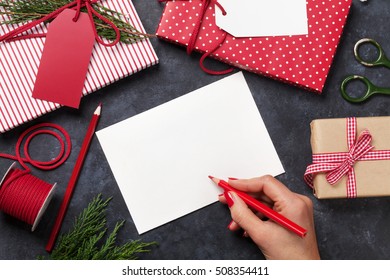 Female Writing Christmas Greeting Card And Gift Wrapping Above Stone Table. Top View With Copy Space