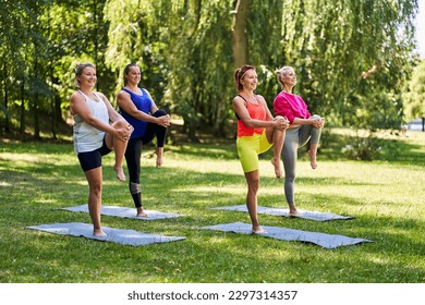 Female yoga class in park during summer. Group of women doing knee to chest pose exercising together - Powered by Shutterstock