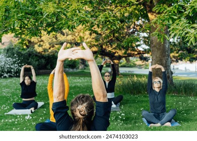 Female yoga class in park. Group of diverse women doing stretching pose exercising together with instructor on green grass lawn. Sport activity for health, wellbeing, mental health. Selective focus - Powered by Shutterstock