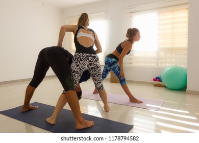 Female Yoga Instructor Adjusts Student In Standing Forward Bend Pose. Yogis Practice Ashtanga Mysore Style. Sports Wear, Training, Professional Help, Challenging, Athletic Concepts