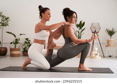 Female yoga instructor helping her student to master a position during private class in the studio. Mental health activity. Two young women doing sport exercises. - Powered by Shutterstock