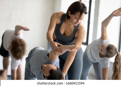 Female yoga trainer helps to man, group training participant, do right perform correctly Extended Side Angle pose, class in sport club studio led by experienced young woman instructor wellness concept - Powered by Shutterstock