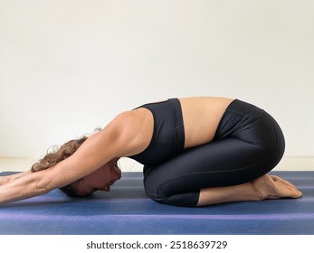 Female yogi with black sports wear in child pose over white background. Hands of woman extended on purple mat at home. Healthy lifestyle, stretching exercise, wellness, balasana, yin yoga concepts - Powered by Shutterstock