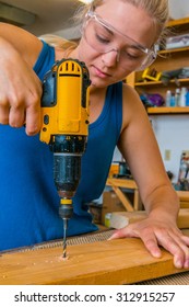 Female Young Adult Woodworker Using Power Drill In Workshop