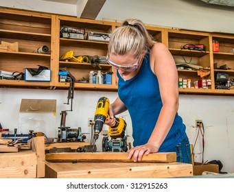 Female Young Adult Woodworker Using Power Drill In Workshop