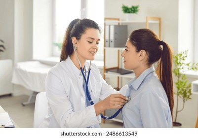 Female young doctor with stethoscope examining woman's lungs, breathing and heartbeat sitting on workplace in exam room during medical checkup in clinic. Health care and medicine concept. - Powered by Shutterstock