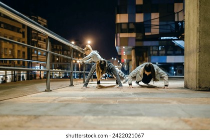 Female young friends sport team doing push ups during training together on the empty city at night - Powered by Shutterstock