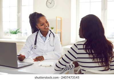 Female young woman patient visiting a smiling friendly african american doctor sitting at the desk in office on her workplace having consultation during medical examination in clinic. - Powered by Shutterstock