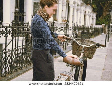 Female young-adult picking her pink bicycle or bike with a basket and a bell parked on the street of the city. Urban non-motorized vehicle with no carbon emissions. Healthy lifestyle. Transport.