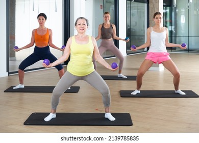 Females of different ages doing pilates exercises with two small fitness balls during group training at gym