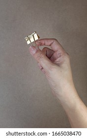 Female's Hand Holding Gold Binder Clip Isolated On Brown Background 