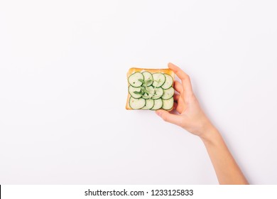 Female's Hand Holding Sandwich Of Green Color, Top View On White Background. Toast With Cucumbers And Sprouts, Flat Lay.