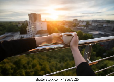 female's hand keeps cup with coffee or tea in hand in rays of sunset; woman on the roof and with cup of hot drink; - Powered by Shutterstock