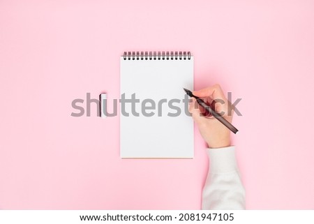 Female's hand writing in white blank open spiral notebook with pen isolated on pastel pink background. Flat lay, copy space. Creative work, business, finance or education concept