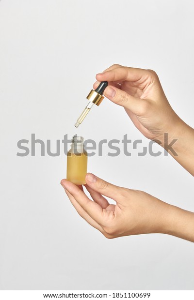 Female\'s hands hold a\
small bottle and pipet of natural medical cannabis essential CBD\
oil against a light grey background, copy space. Use of cannabis\
for medical purposes.