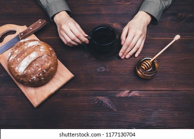 Female's hands holding cup of tea or coffee on dark wooden table, top view. Simple rural breakfast with honey and rye bread. - Powered by Shutterstock