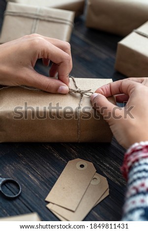 Female's hands in pullover enveloping Christmas gift box decorated with kraft paper