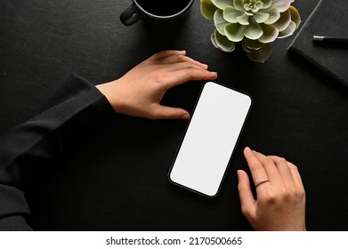 A Female's Hands Using A Mobile Phone Touchscreen At Her Stylish Black Workspace Tabletop. Overhead View And Close-up Image Of A Cellphone White Screen Mockup.