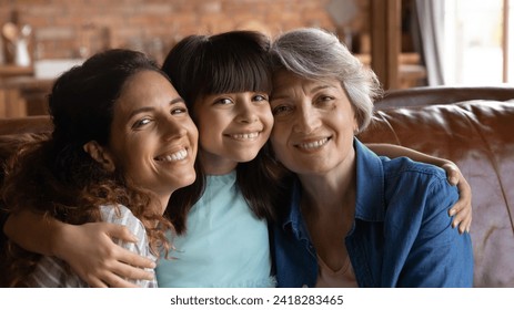 Females relatives. Portrait of 3 generations latin family mature grandmother adult mother preteen child daughter granddaughter cuddle on couch look at camera. Happy little girl hug mommy and grandma - Powered by Shutterstock