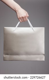 A Female(woman) Hand Hold A Gold Shopping Bag(paper Bag) And White Strings At The Studio.