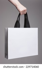 A Female(woman) Hand Hold A White Shopping Bag(paper Bag) And Black Strings At The Studio.