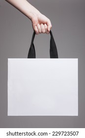 A Female(woman) Hand Hold A White Shopping Bag(paper Bag) And Black Strings At The Studio.