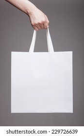 A Female(woman) Hand Hold A White Shopping Bag(paper Bag) And White Strings At The Studio.