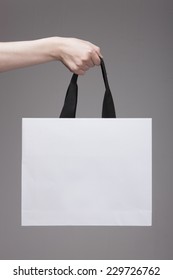 A Female(woman) Hand Hold A White Shopping Bag(paper Bag) And Black Strings At The Studio.