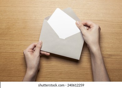 Eine Frau hält einen Umschlag und eine Postkarte auf dem Holzschreibtisch, Draufsicht im Studio. 