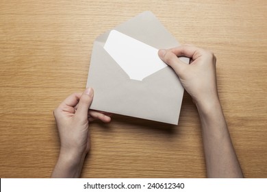 A Female(woman) Hand Hold(open) A Envelope And Post Card On The Wood Desk, Top View At The Studio. 