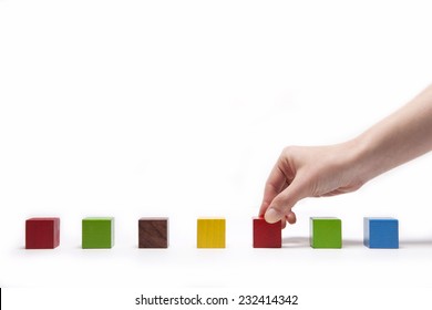 A Female(woman) Hand Pick Up(hold) A Wood Block Among Many Color(red, Green, Blue, Yellow) Wood Blocks Isolated White At The Studio.