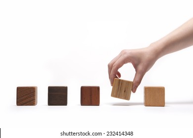 A Female(woman) Hand Pick Up(hold) A Wood Block Among Many Wood Blocks(oak, Walnut, Teak, Cherry) Isolated White At The Studio.