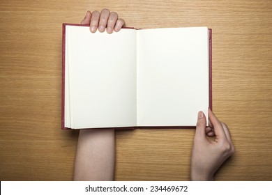 A Female(woman) Hands Hold A Blank(empty) Book(note, Diary) On The Wood Desk(table), Top View At The Studio.