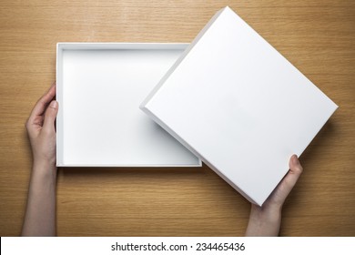 A Female(woman) Hands Hold A Empty(blank) White Box On The Desk(table) Top View At The Studio.