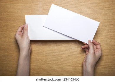 A Female(woman) Hands Hold A Empty(blank) White Letter And Envelope On The Desk(table), Top View At The Studio.