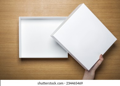 A Female(woman) Hands Hold A Empty(blank) White Box On The Desk(table) Top View At The Studio.