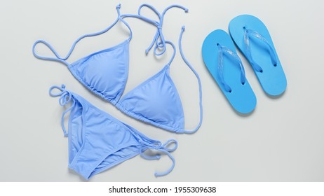 Feminine beach accessories bikini swimsuit and flip flops on a gray background. Top view, flat lay. Blue swimwear and blue beach shoes. Summer travel concept. Banner.
