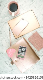 Feminine Desk Workspace With Rose Gold Accessories On White Marble Table, Flatlay Overhead.