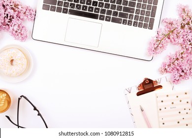 Feminine desktop, close up of laptop keyboard, blank clipboard, coffee & donut, lilac flowers. Flat lay composition, notebook computer, cappuccino cup, glasses eye wear, white background. Copy space.