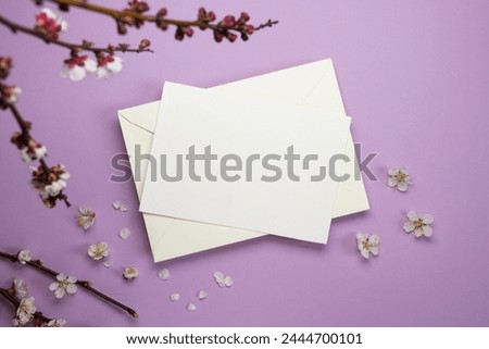 Feminine desktop mockup scene with blossoming tree branches and blank paper greeting card on a purple background. Flat lay, top view. Space for text. Mock up.
