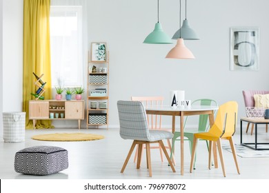 Feminine Dining Room Interior With Colorful Chairs At The Round Table And Wooden Cupboard Near The Window With Yellow Drapes