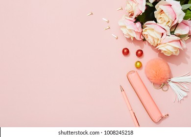Feminine flat lay with roses, pen, fashion accessory and chocolates on pink background