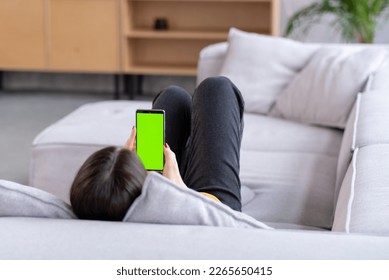 Feminine Hand Scrolling Feed on Smartphone with Green Screen Mock Up Display. Female is Relaxing on Sofa at Home, Watching Videos and Reading Social Media Posts on Mobile Device. - Powered by Shutterstock